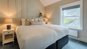 A bedroom with a large bed, two bedside tables, a nightstand, a window with a view of a road, and a radiator.