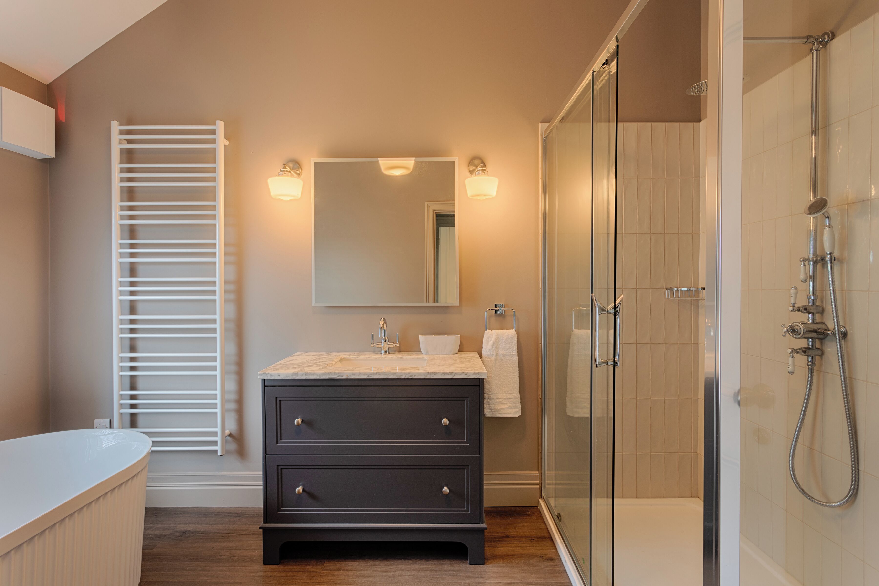 A modern bathroom with a glass-enclosed shower, a dark vanity with a mirror, and a white bathtub.