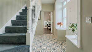 A hallway with a staircase, patterned floor, and a window with a plant.