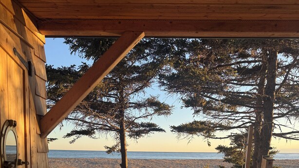 A wooden deck leading to a cabin with a view of a lake and trees. - Lawrencetown Beach House with Hot Tub & Sauna (Head of Chezzetcook)