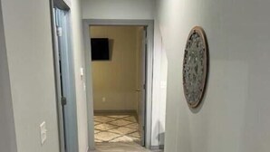 A narrow hallway with a trash bin on the left, a door at the end, and a patterned floor. - Hidden gem (Blanchard)
