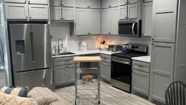 A modern kitchen with grey cabinets, a stainless steel refrigerator, a microwave, and a ceiling fan. - Hidden gem (Blanchard)