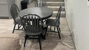 A dining area with a round table and four chairs, a staircase leading to another floor, and a hallway with a door and a trash can. - Hidden gem (Blanchard)