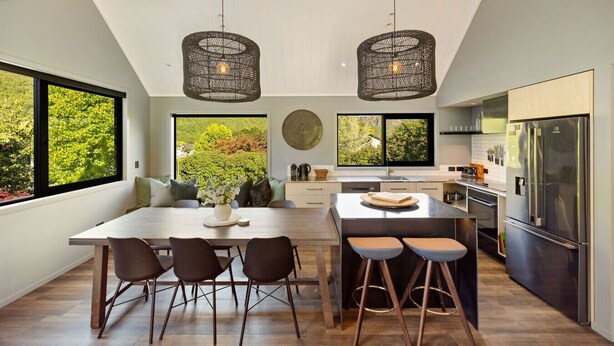 A modern kitchen with a large island, pendant lights, and a view of greenery.