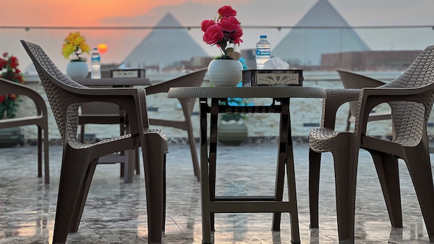 A table with chairs and a vase of flowers, a water bottle, and a tissue box, with pyramids in the background. - Luxury jacuzzi & pyramids view  (Giza)
