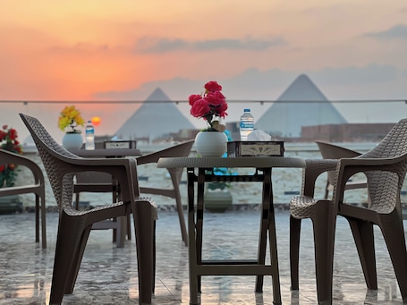 A table with chairs and a vase of flowers, a water bottle, and a tissue box, with pyramids in the background.