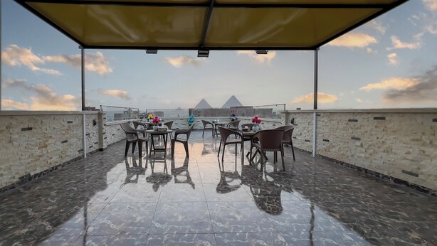 A terrace with a view of the pyramids, covered seating, and a stone wall.