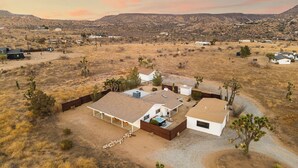 Une maison moderne dotée d’un vaste patio, entourée d’un paysage aride et vallonné.