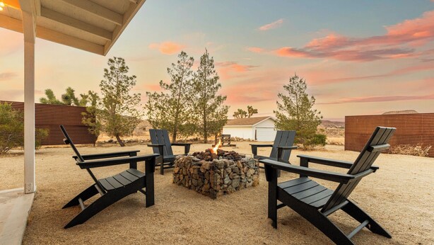 Un espace patio aménagé avec quatre chaises Adirondack noires disposées autour d’un foyer en pierre.