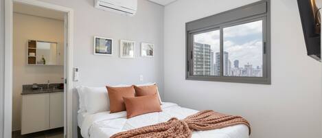 Une chambre moderne avec un lit, une fenêtre donnant sur la ville, un climatiseur intégré et une petite kitchenette.
