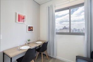 A dining area with a table set for two, two chairs, a vase with a plant, and two framed artworks on the wall. - AD330 (São Paulo)