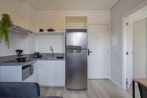 Ett kompakt kök med ett inbyggt kylskåp, en mikrovågsugn och en liten arbetsyta med en kaffebryggare.