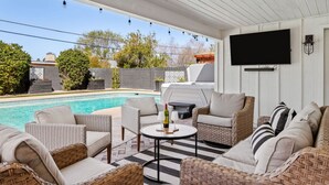 An outdoor patio with wicker furniture, a pool, and a flat-screen TV.