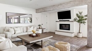 A modern living room with a sofa, coffee table, fireplace, TV, and a plant.