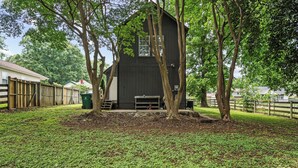 A black building with a small porch and a window, surrounded by trees and a grassy yard. - Cozy Urban Getaway - 3BR 1.5BA - 7 Mins to Downtown CLT (Charlotte)