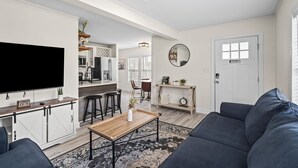 A modern living room with a flat-screen TV, dark sofas, a wooden coffee table, and a patterned rug. - Cozy Urban Getaway - 3BR 1.5BA - 7 Mins to Downtown CLT (Charlotte)