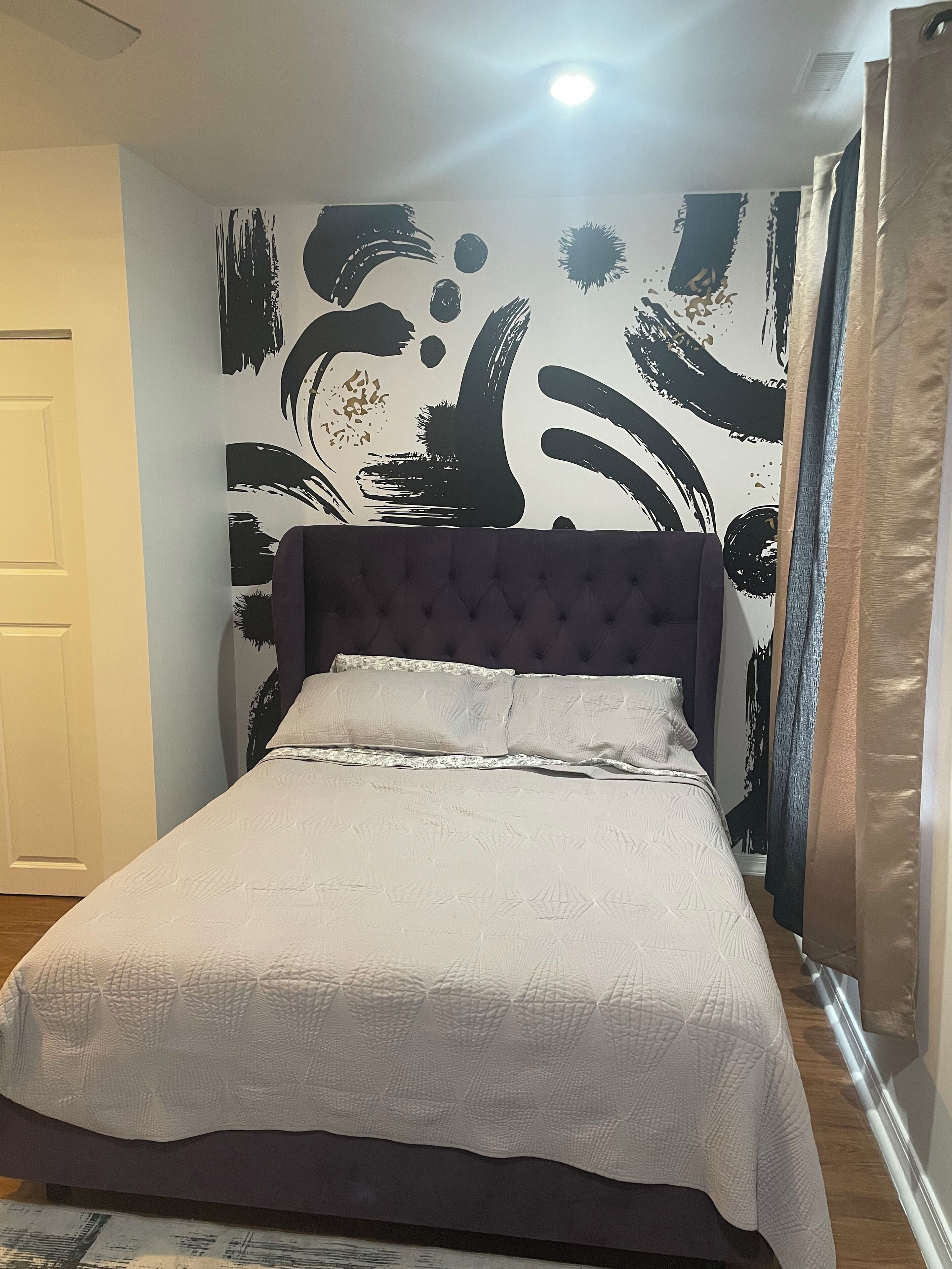 Un dormitorio con cama, cabecera oscura y pared con arte abstracto en blanco y negro.