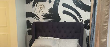 Un dormitorio con cama, cabecera oscura y pared con arte abstracto en blanco y negro.