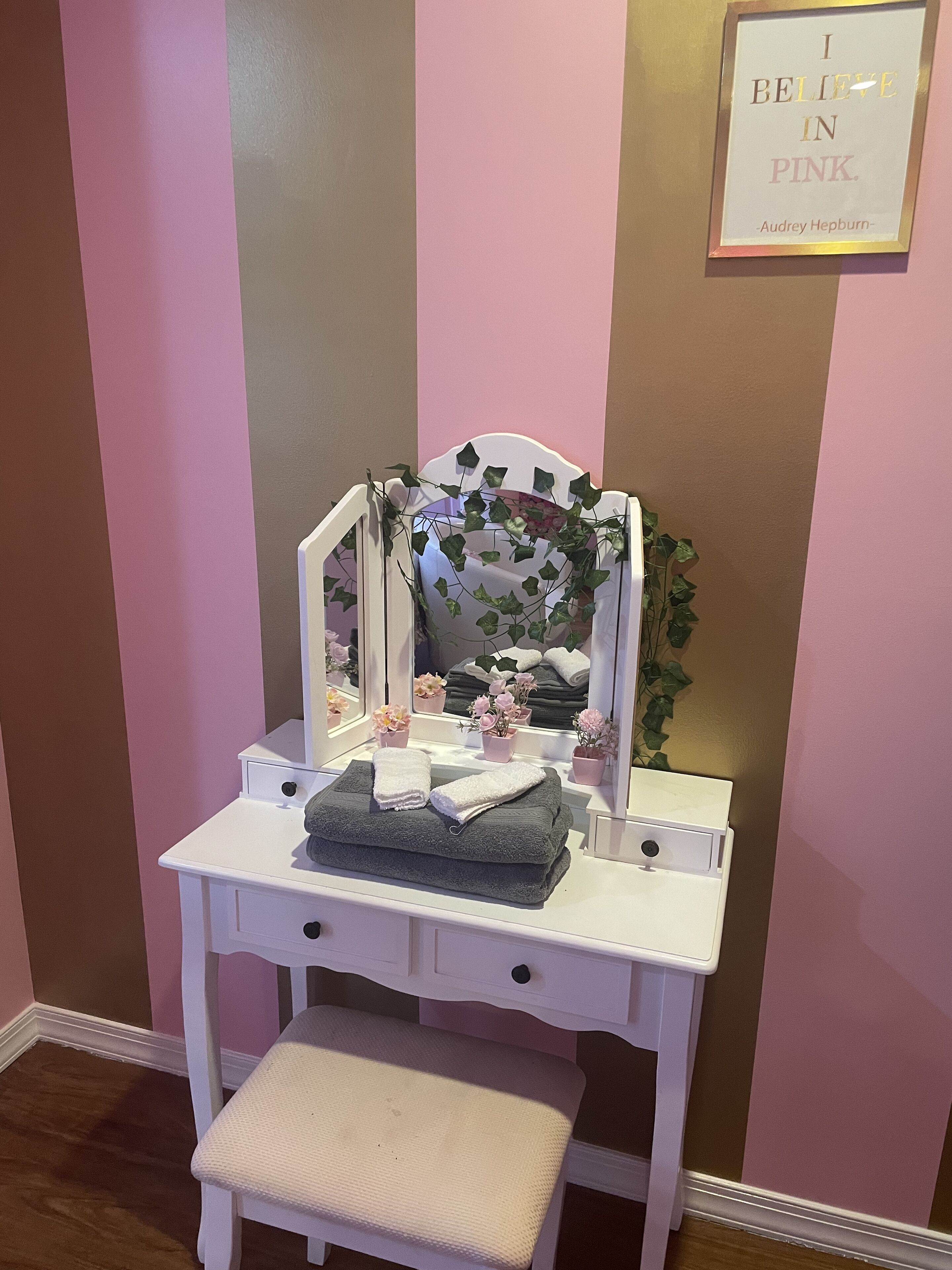 A vanity with a mirror, a bench, and a framed quote on the wall.