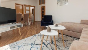 A modern living room with a flat-screen TV, a blue and white rug, a round coffee table, a blue armchair, and a beige sofa. - Stylish Budva Apt withPanoramic View-2Bedroom Apt (Budva)