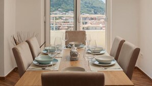 A dining area with a table set for four, a view of a mountainous landscape through large windows, and a balcony with a railing. - Stylish Budva Apt withPanoramic View-2Bedroom Apt (Budva)