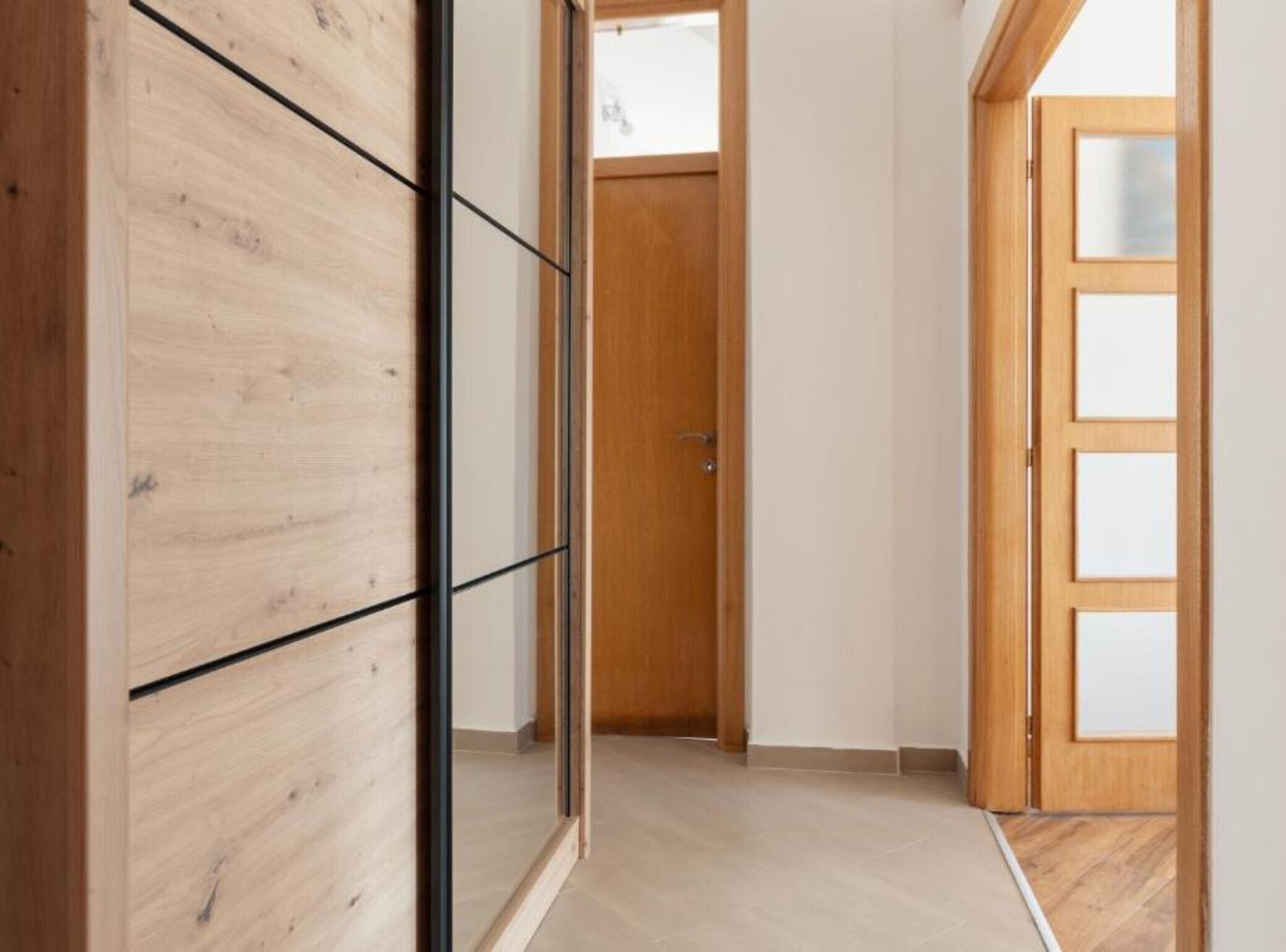 Ein Korridor mit Holzboden, einer Holztür mit Glasfeldern und einer Schiebetür aus Holz.