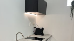 Een kleine keuken met een spoelbak, een koffiezetapparaat en een zwart kastje boven het aanrecht.