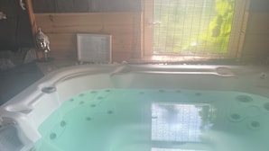 Een hottub met bedieningspaneel, omringd door houten wanden en een raam met zonwering.
