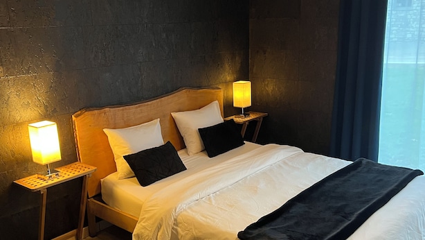 Hotelkamer met een groot bed, twee nachtkastjes met lampen, donkere muren en uitzicht op een gebouw door een raam.
