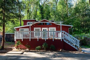 A red building with a white balcony and stairs, surrounded by trees.