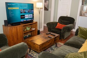 A living room with a flat-screen TV on a wooden stand, a sofa, a coffee table, and a lamp.
