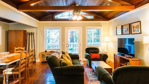 Una sala de estar con techo de madera, un comedor con mesa y sillas, un sofá y una televisión.