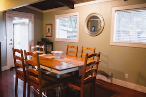 A dining area with a wooden table and chairs, a white vase, and a framed picture on the wall.