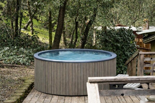 A hot tub in a wooded area with a wooden deck and a fence.