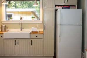 A kitchen with a double sink, a stainless steel kettle, a white refrigerator, and a window with plants on the windowsill.