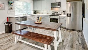 A modern kitchen with white cabinets, stainless steel appliances, and a wooden dining table with benches.