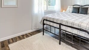 A bedroom with a bed, white walls, a wooden ceiling, and a window with curtains.