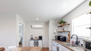 Cozinha moderna com armários brancos, bancada de madeira e forno embutido. Há uma janela com persianas, micro-ondas e cafeteira no balcão.