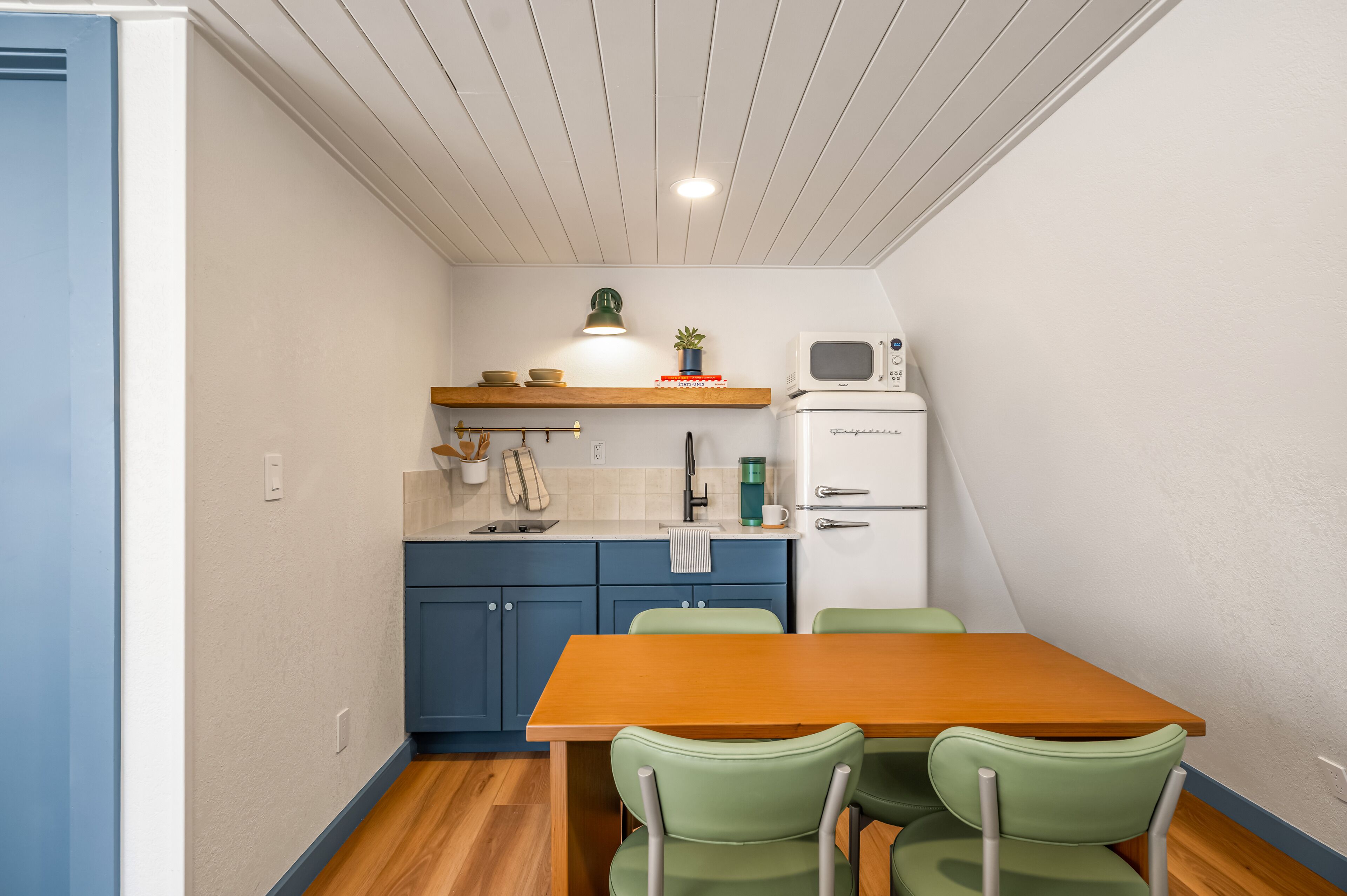 A compact kitchen with a wooden table, green chairs, a microwave, and a small refrigerator.