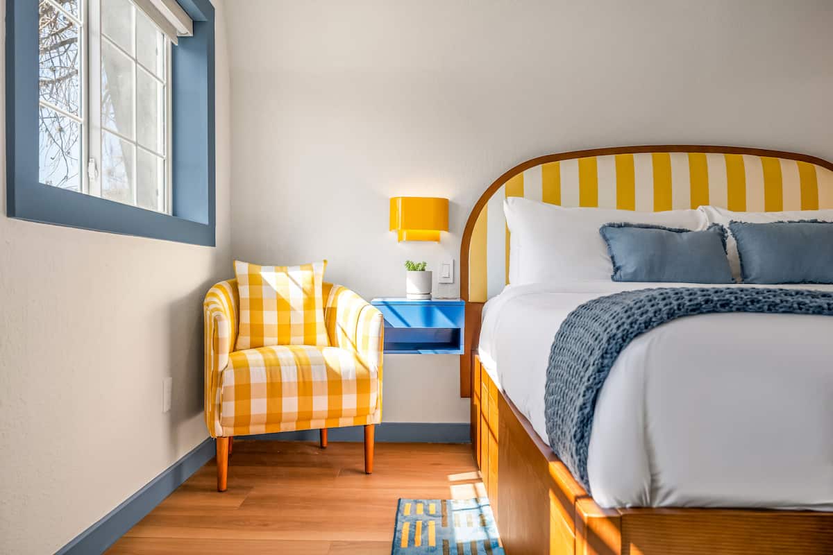A bedroom with a bed, a chair, a nightstand, and a window.