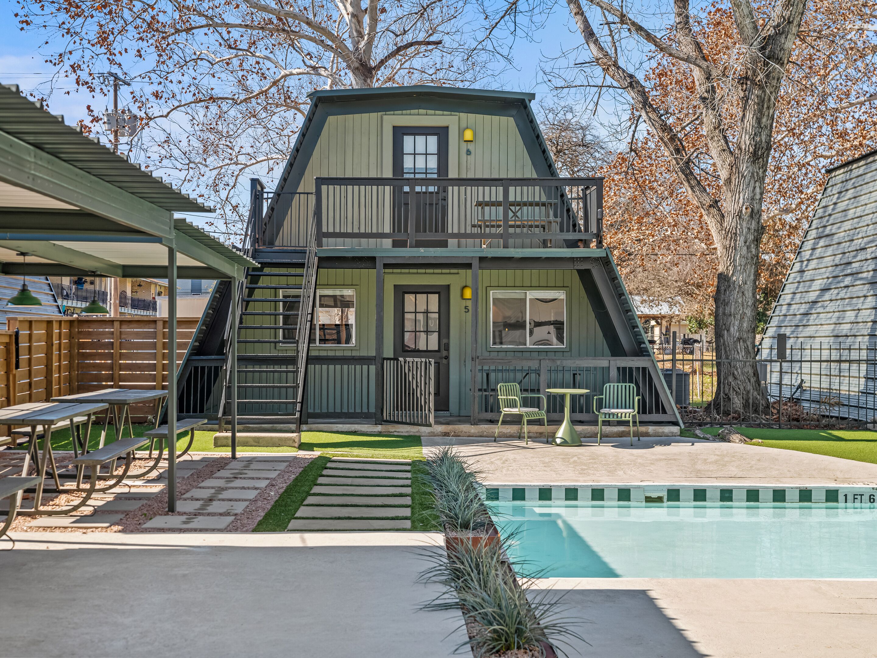 A two-story building with a balcony, a pool, and outdoor seating.