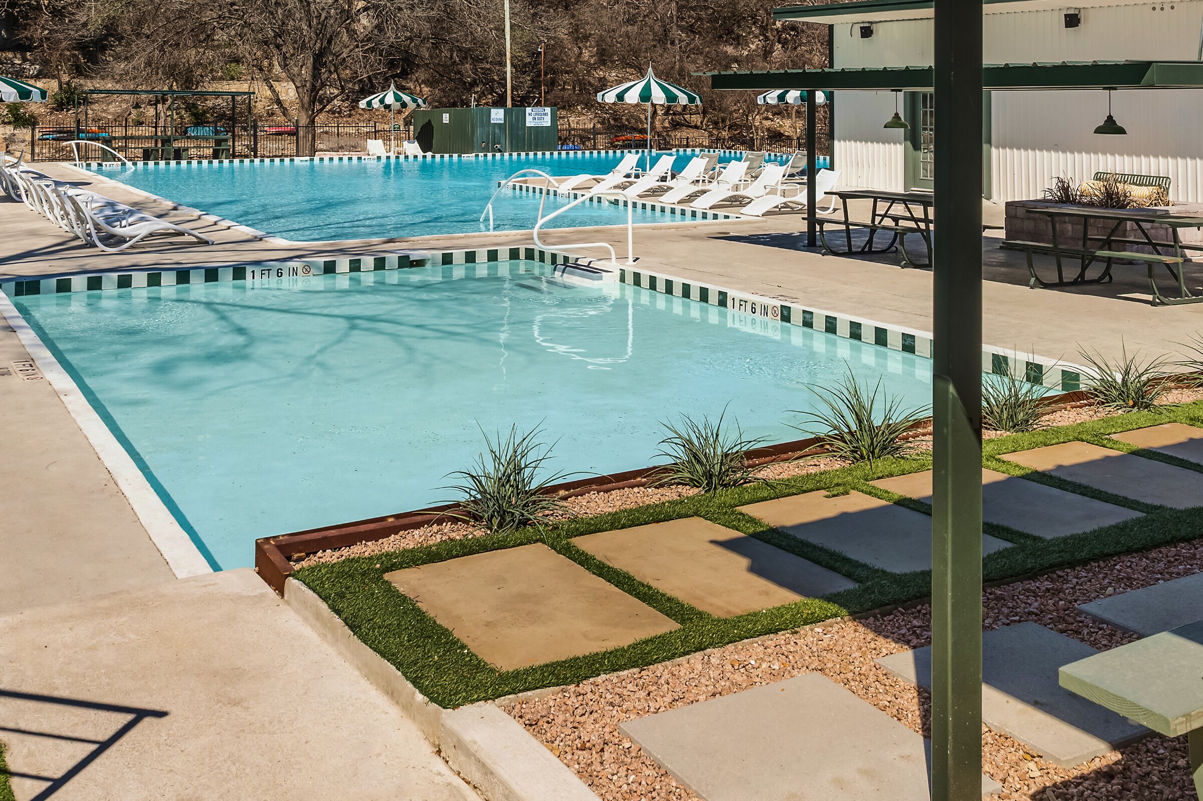 A rectangular swimming pool with a 1 ft 6 in depth, surrounded by lounge chairs and picnic tables.