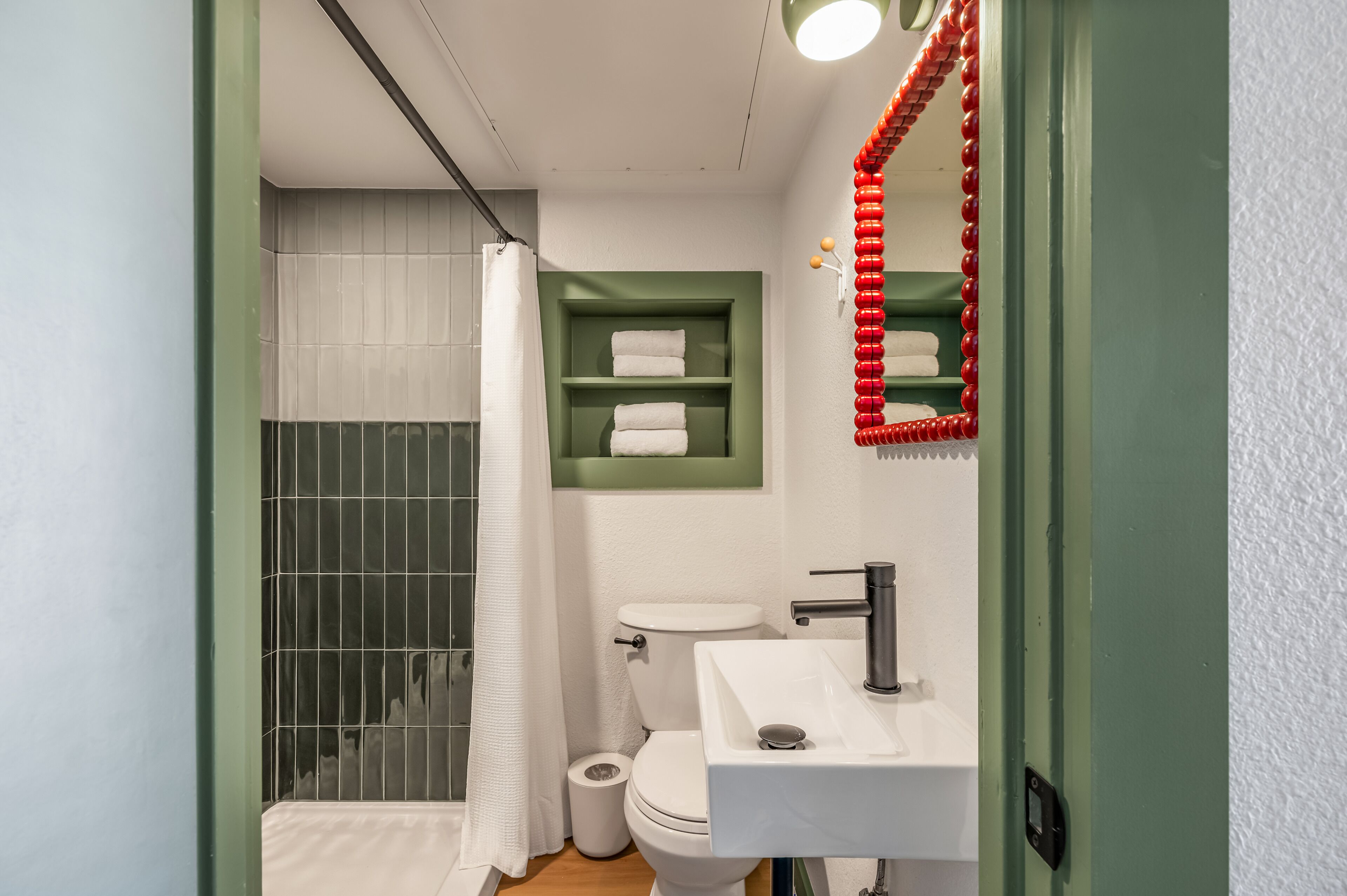 Une salle de bain avec un lavabo blanc, des étagères vertes, des toilettes blanches et un rideau de douche.
