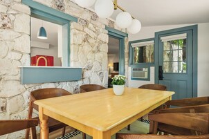 A dining area with a stone wall, wooden table, chairs, a potted plant, and a red appliance in the background.