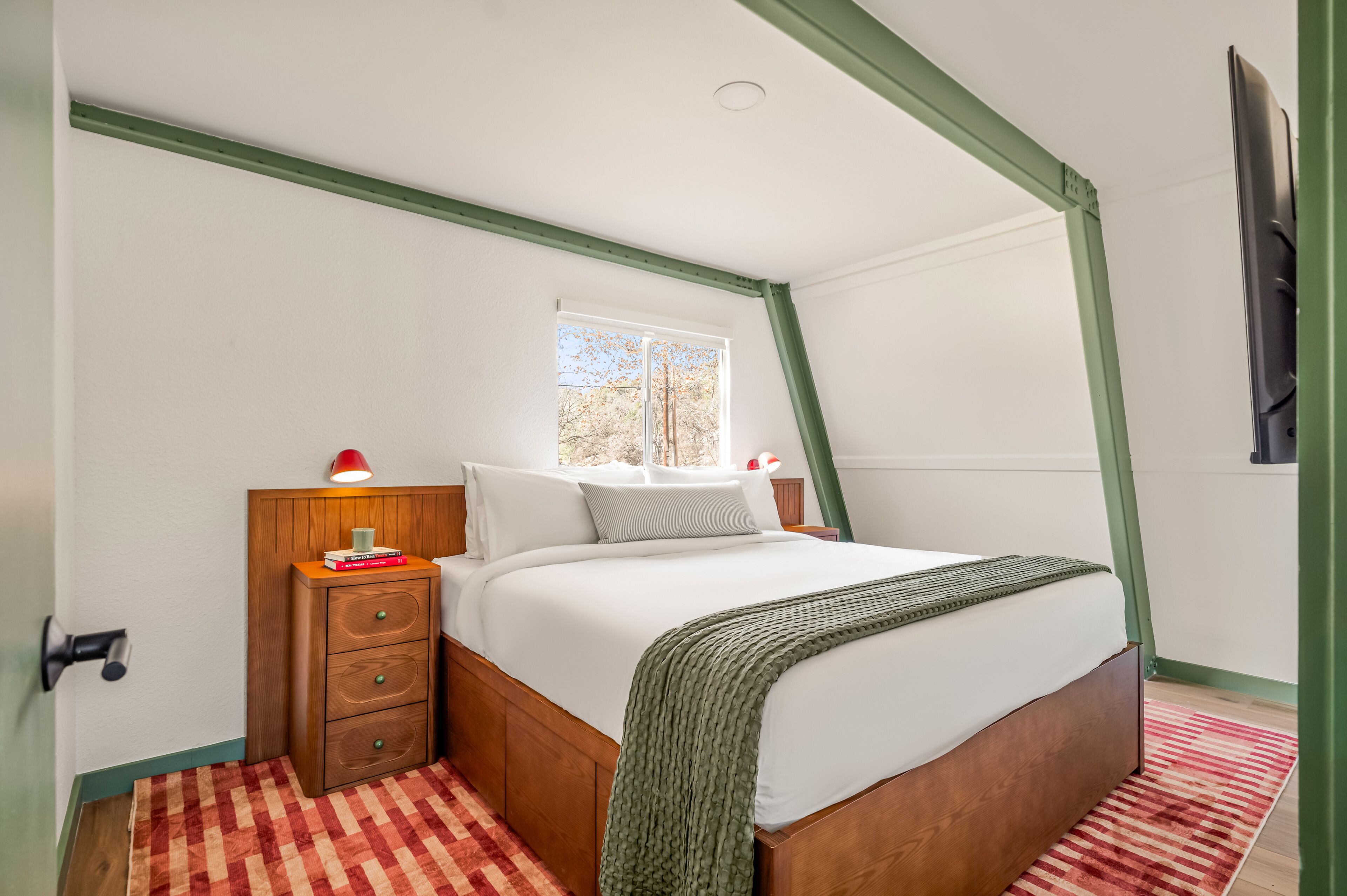 A bedroom with a bed, a nightstand, a lamp, and a window.