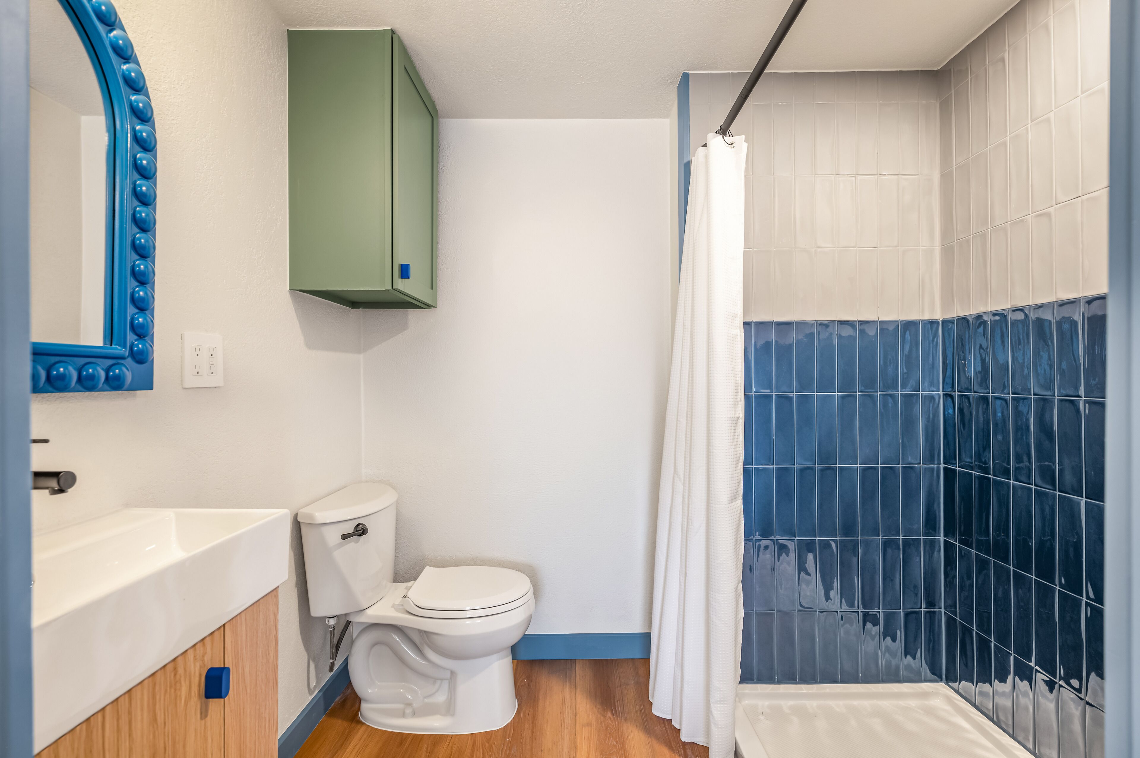 Een badkamer met een wit toilet, een groen kastje en een douchegedeelte met blauwe tegels.