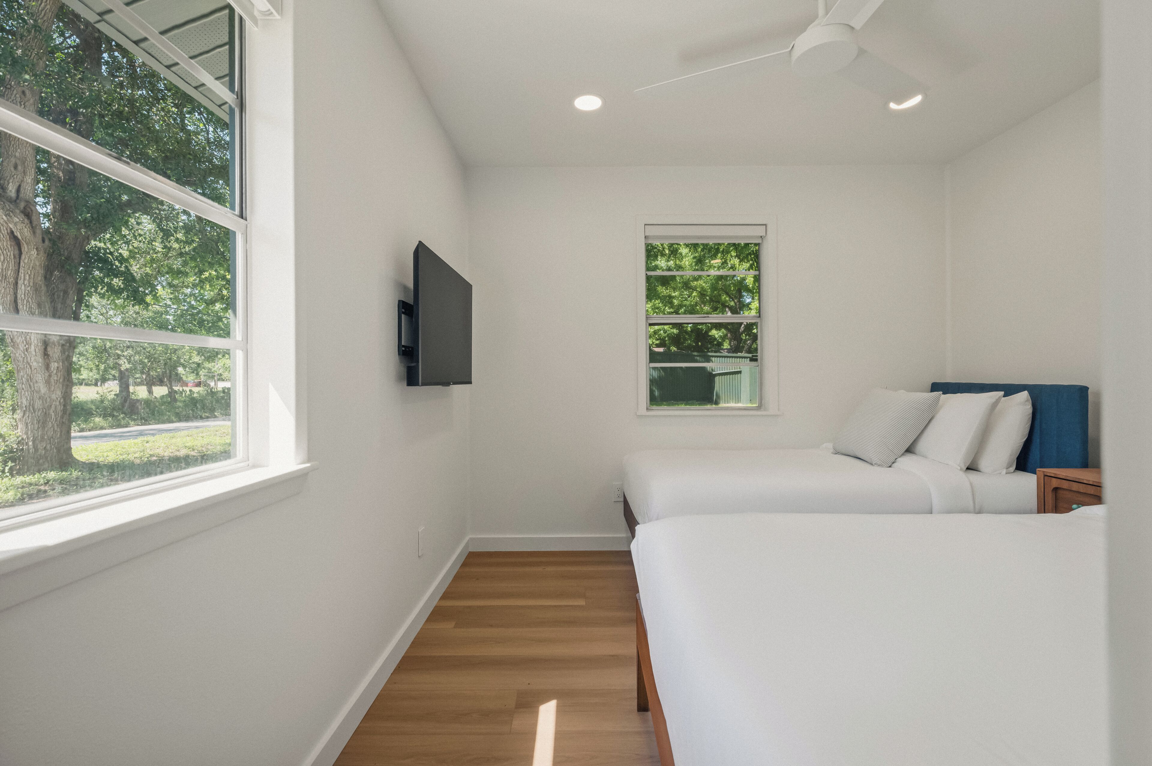 A bedroom with a TV, a window, a ceiling fan, and a bed.