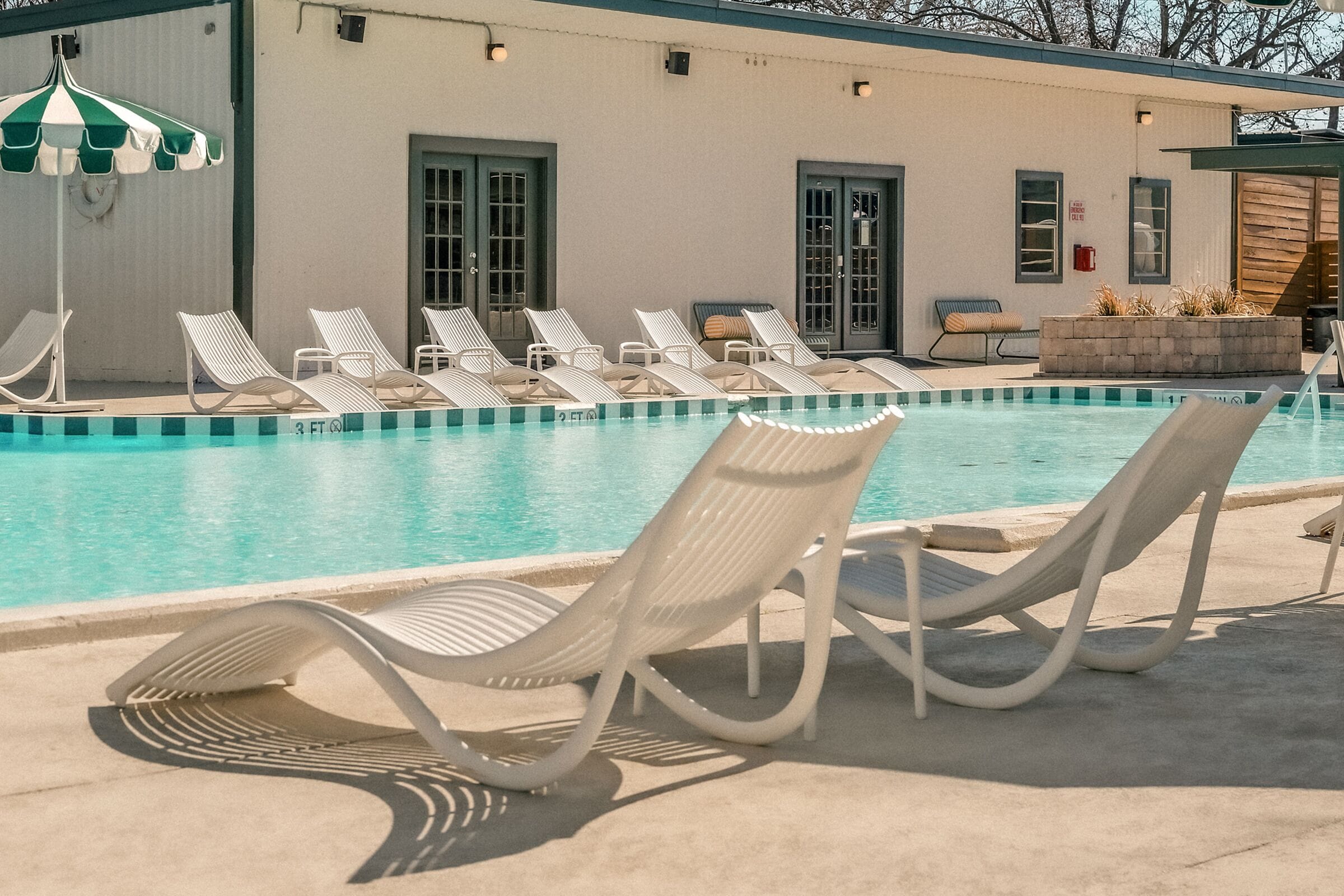 A pool area with lounge chairs and a building with doors and windows.