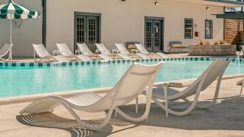 A pool area with lounge chairs and a building with doors and windows.