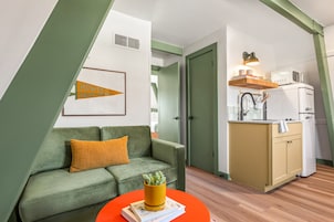 Um apartamento moderno com um sofá verde, uma pequena cozinha com micro-ondas e um quadro na parede.